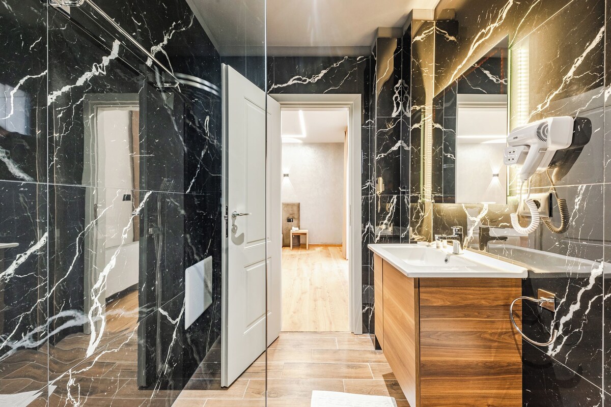 Un baño moderno con paredes de mármol, un mueble de tocador de madera y un secador de pelo montado en la pared.
