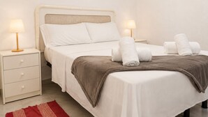 Un letto rifatto con lenzuola bianche, due lampade ai lati del letto, una coperta marrone e asciugamani arrotolati su un lato.