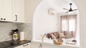 A modern kitchen with a marble backsplash, a built-in oven, and a window overlooking a living area with a sofa and curtains. - Charming House with Nature (El Chaparral)