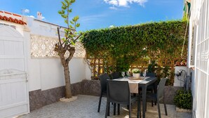 Un patio con tavolo e sedie, circondato da un recinto bianco e un siepe verde.