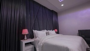 A modern bedroom with a large bed, dark curtains, and a small bedside table with a lamp. - 3H VILLAS HOTEL & LUXURY SHORT-LET  (Lekki)
