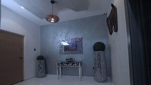 A modern hallway with a grey wall, a decorative mirror, a small table with decorative items, and two patterned planters. - 3H VILLAS HOTEL & LUXURY SHORT-LET  (Lekki)