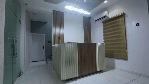 A reception area with a modern design, featuring a reception desk, a glass partition, and an air conditioning unit on the wall. - 3H VILLAS HOTEL & LUXURY SHORT-LET  (Lekki)