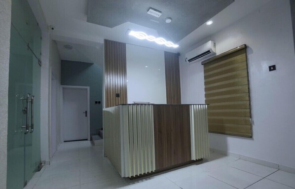 A reception area with a modern design, featuring a reception desk, a glass partition, and an air conditioning unit on the wall.