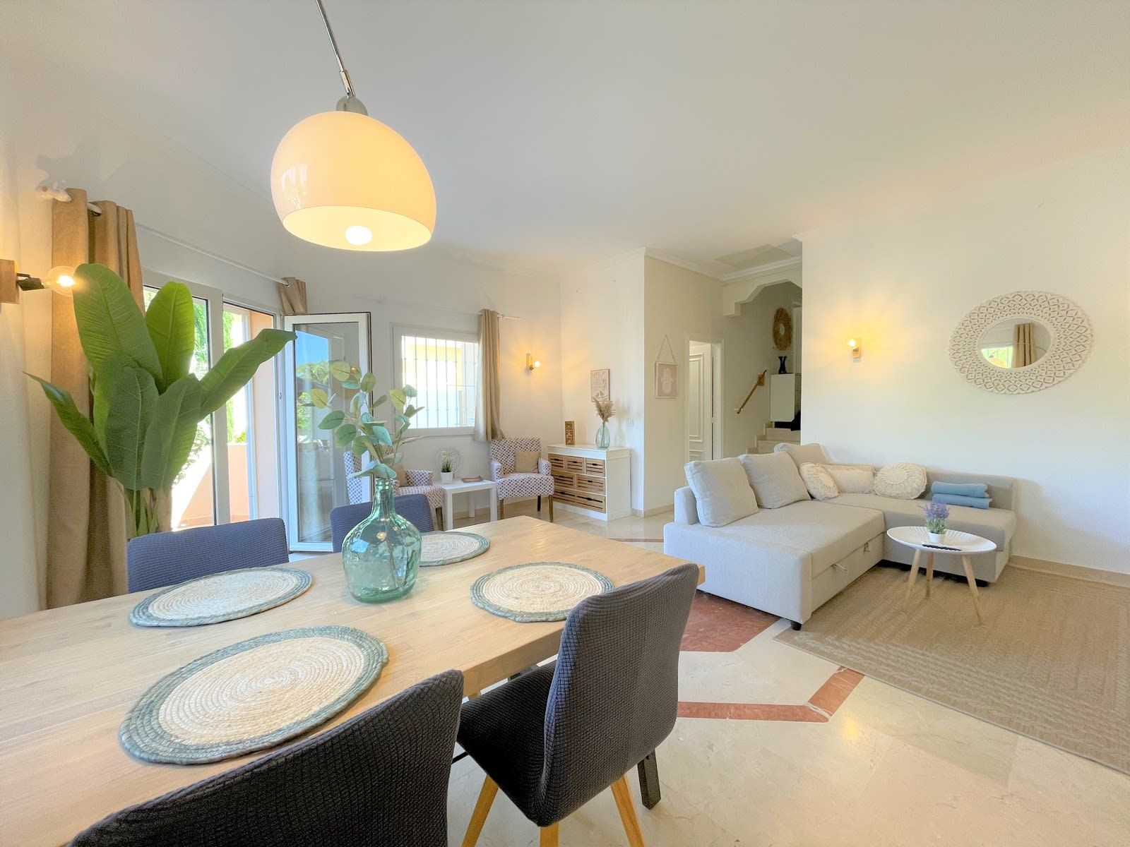 A modern living space with a dining area, a sofa, and a staircase leading to an upper level.