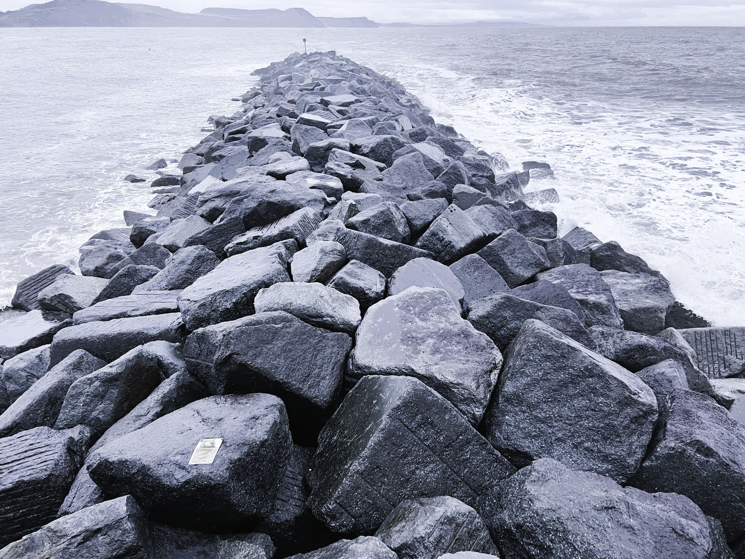 A rocky breakwater extending into the sea with a distant landmass visible in the background.