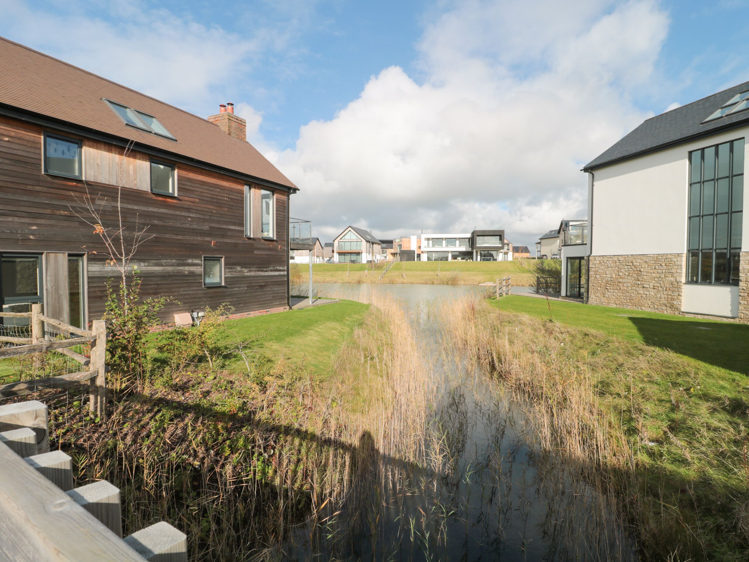 Un quartier résidentiel avec des maisons modernes, un petit étang et une clôture en bois.