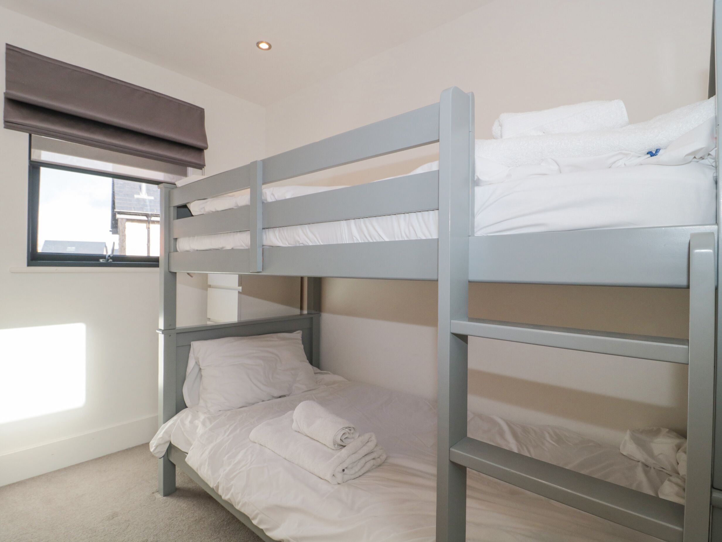 A bunk bed room with white bedding and a window with a view of buildings outside.