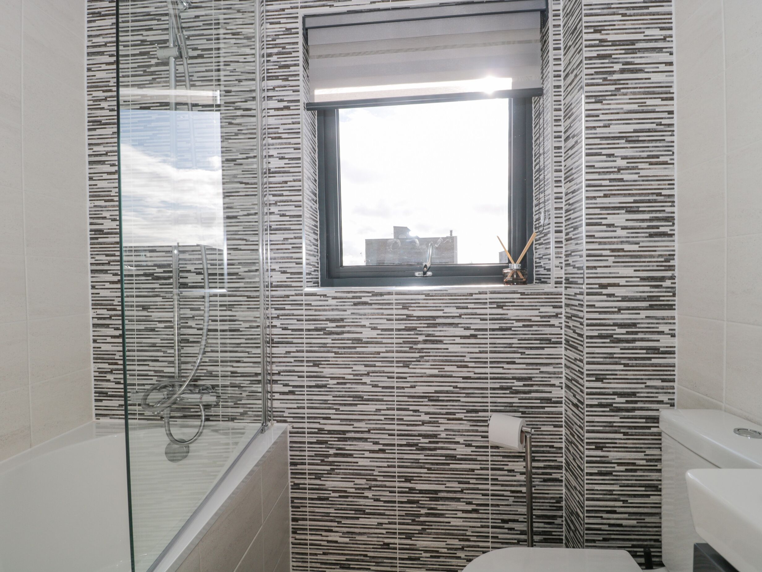 Ein modernes Badezimmer mit Duschkabine aus Glas, Toilette und Fenster mit Blick auf Gebäude.