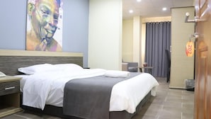 Una habitación de hotel con cama, escritorio, silla, un cuadro en la pared y una puerta con un letrero de número.