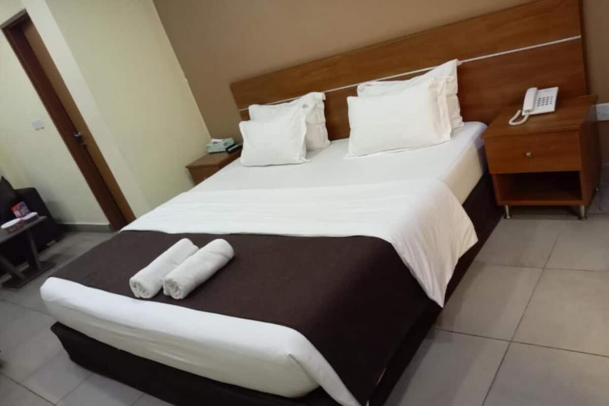 A neatly made bed with white linens and a brown headboard, a bedside telephone, and a small bedside table with a lamp.
