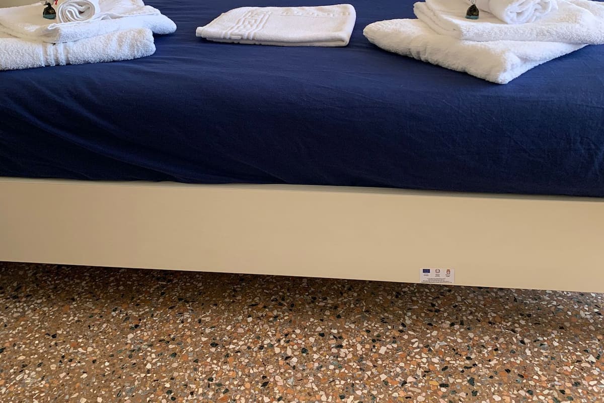 A hotel room with a bed, white pillows, a blue bedspread, and neatly folded white towels on the bed.