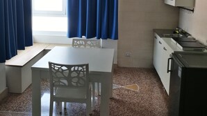 A compact kitchen with a white table and chair, a built-in sink, and a refrigerator. - settimo sole affittacamere (Taranto)