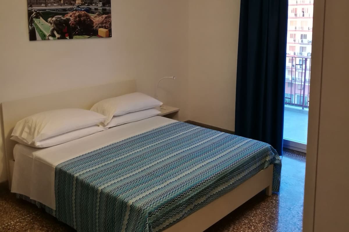 A hotel room with a bed, a hanging light fixture, a window with curtains, and a wall-mounted picture.