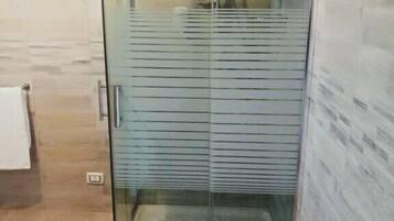 A glass-enclosed shower area with a tiled floor and a wooden wall.