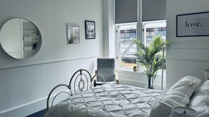 A bedroom with a bed, a chair, a round mirror, and a window with blinds. - Beautiful one bed Apartment in Glasgow West End (Glasgow)