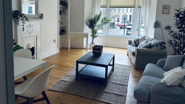 A living room with a fireplace, a sofa, a coffee table, and a view of the street through large windows. - Beautiful one bed Apartment in Glasgow West End (Glasgow)