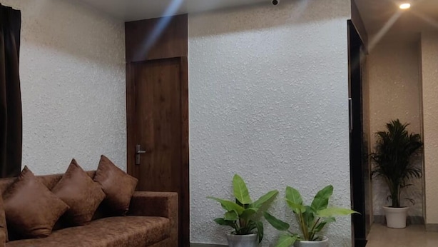 A modern living room with a ceiling fan, a brown sofa, and two potted plants. - Hotel Daisy (Guwahati)