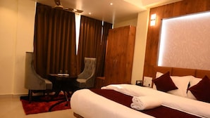 A hotel room with a large bed, a desk, a chair, and a wardrobe. - Hotel Daisy (Guwahati)