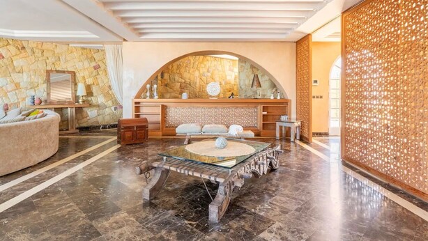 A spacious lobby with a stone wall, a round glass table, and a seating area with a sofa and armchairs.