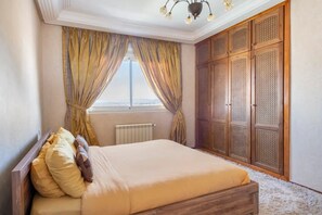A bedroom with a bed, a window with curtains, a radiator, and a wardrobe. - Haddad's luxurious villa with an amazing view and swimming pool (Tangier)