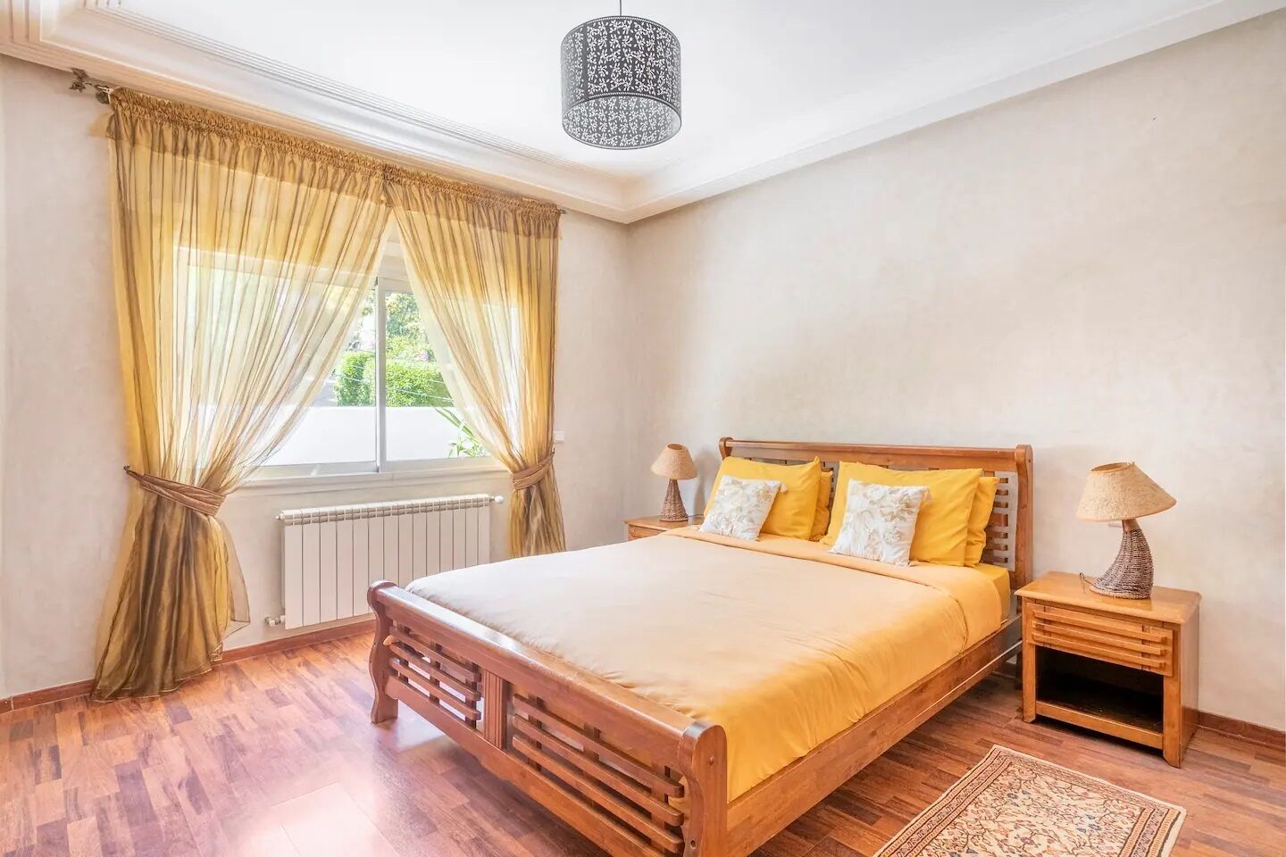 A bedroom with a wooden bed, yellow bedding, a nightstand with a lamp, and a window with curtains.