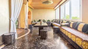 A spacious lounge with a long bench, a central table, and a ceiling with wooden beams and a hanging light fixture.