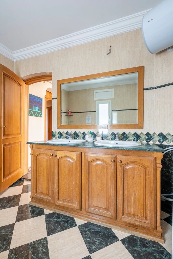 Una cocina con armarios de madera, piso de mármol y un espejo grande sobre el lavamanos.