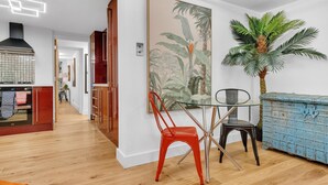 Une cuisine moderne avec un plancher en bois, une chaise rouge, une table en verre et un meuble bleu.