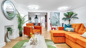 Un salon moderne avec des canapés orange, une table basse sur laquelle sont posées des boissons et un grand miroir au mur.