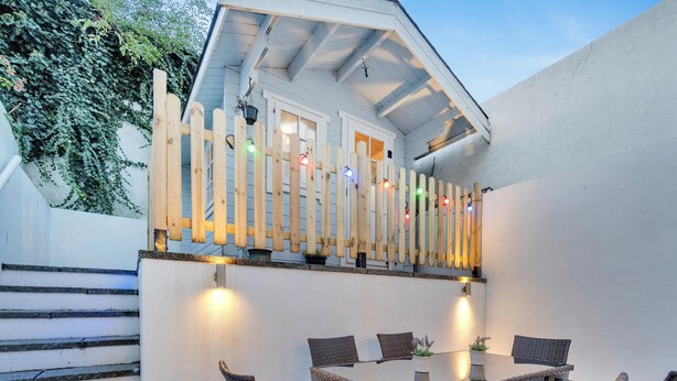 Un espace patio aménagé avec des meubles en osier, une clôture blanche et des guirlandes lumineuses.