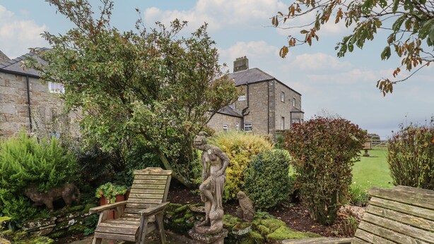 A garden with stone benches, a statue, and a stone building in the background. - The Barn (Morpeth)