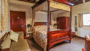 A four-poster bed with floral bedspread, a wooden wardrobe, a small round table with a lamp, and a sofa with a cushion. - The Barn (Morpeth)