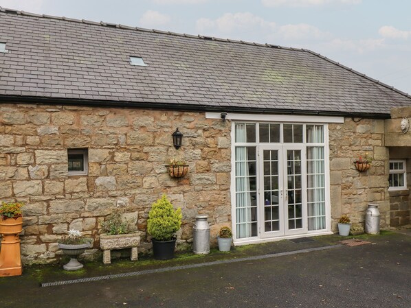 A stone building with a large window and a door, surrounded by potted plants and a stone bench.