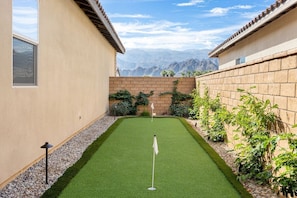 Un green de golf, avec un mât de drapeau, entouré d’un mur de briques et de végétation.