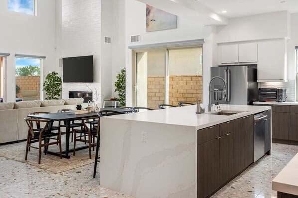 A modern kitchen with a large island, dark cabinetry, stainless steel appliances, and a view to the backyard.