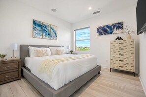 A modern bedroom with a large bed, a bedside table, a wardrobe, and artwork on the walls. - Desert Oasis Retreat | EV Charger, GolfCourseViews (La Quinta)