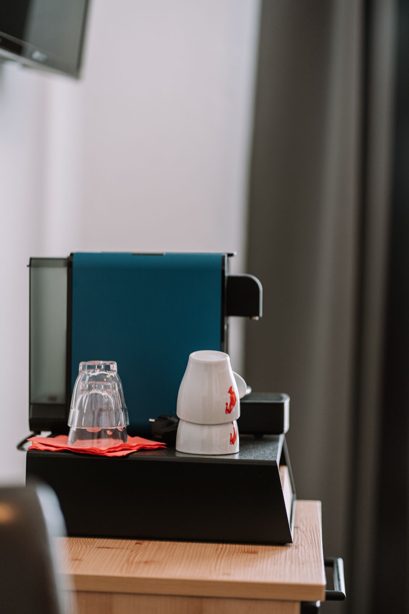 Une machine à café, un verre et une tasse sur une table, avec une serviette rouge.