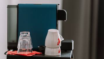 Une machine à café, un verre et une tasse sur une table, avec une serviette rouge.