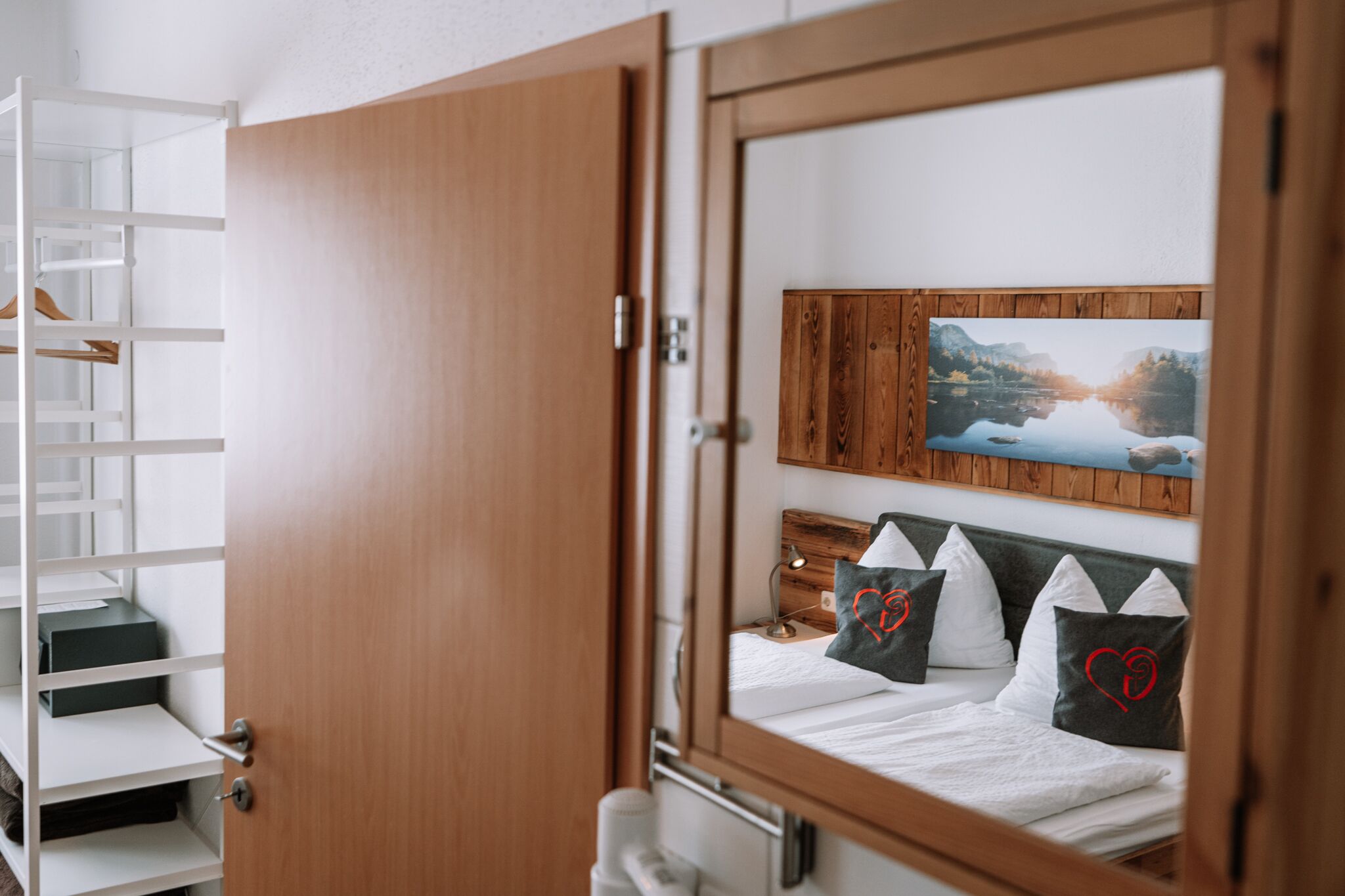 Un dormitorio con puerta de madera, una cama con ropa de cama blanca y un cuadro de un paisaje en la pared.