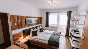 Une chambre à coucher avec une tête de lit en bois, un lit recouvert de linge de maison blanc, une table de chevet avec une lampe, une fenêtre avec des rideaux et une armoire intégrée.