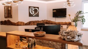 Un espace d’accueil avec un comptoir de réception en bois, un téléviseur fixé au mur, un panneau en forme de cœur et un mur décoré sur le thème de la montagne.