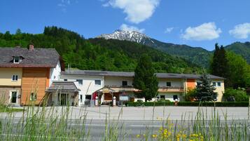 A hotel with a mountain backdrop, featuring a parking lot and a building with a sloped roof.