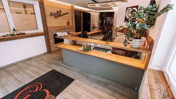 Un espace d’accueil avec un comptoir de réception en bois, une plante aux feuilles rayées de noir et de blanc, et un panneau d’accueil.