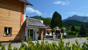 Un bâtiment en bois avec une façade en pierre, un espace extérieur aménagé pour s’asseoir et une vue sur les montagnes.
