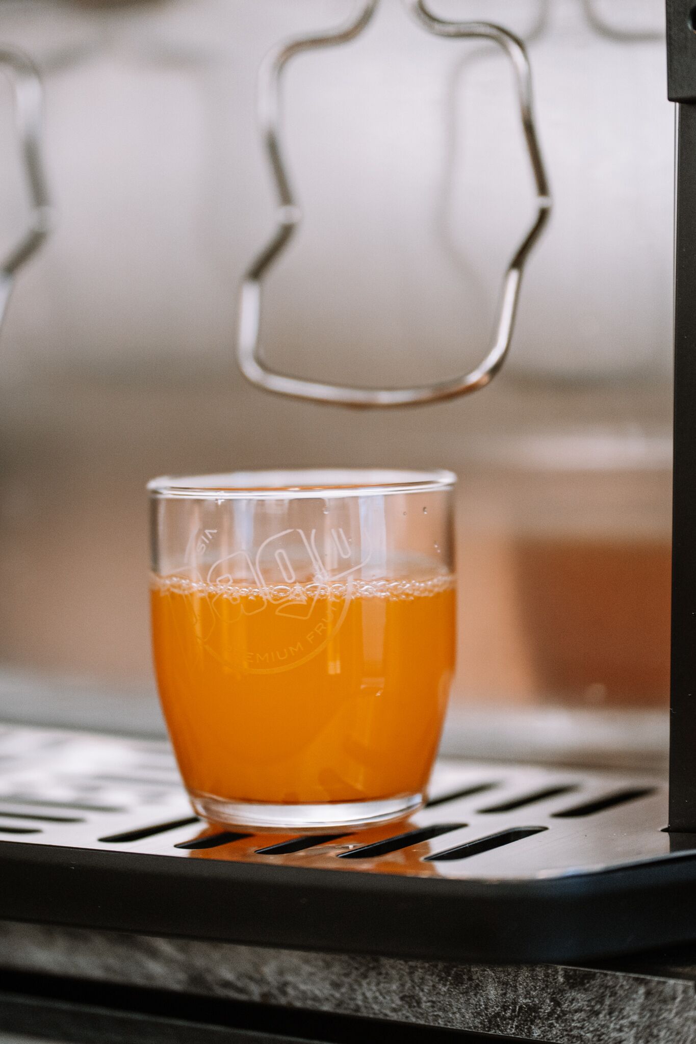 A glass of orange juice on a metal surface with a blurred background.