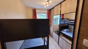 A compact room with a bunk bed, a small table, and a window with curtains.