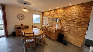 A cozy kitchen with a wooden table and chairs, a stone wall backsplash, and a clock on the wall.