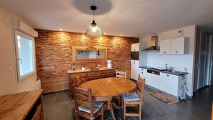A modern kitchen with a wooden wall backsplash, a round dining table with chairs, and a pendant light.