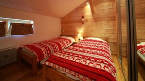 Ett mysigt rum med träväggar och ett sluttande tak. Det finns två sängar med rött och vitt sänglinne, ett litet sängbord med en lampa och ett fönster med gardiner.
